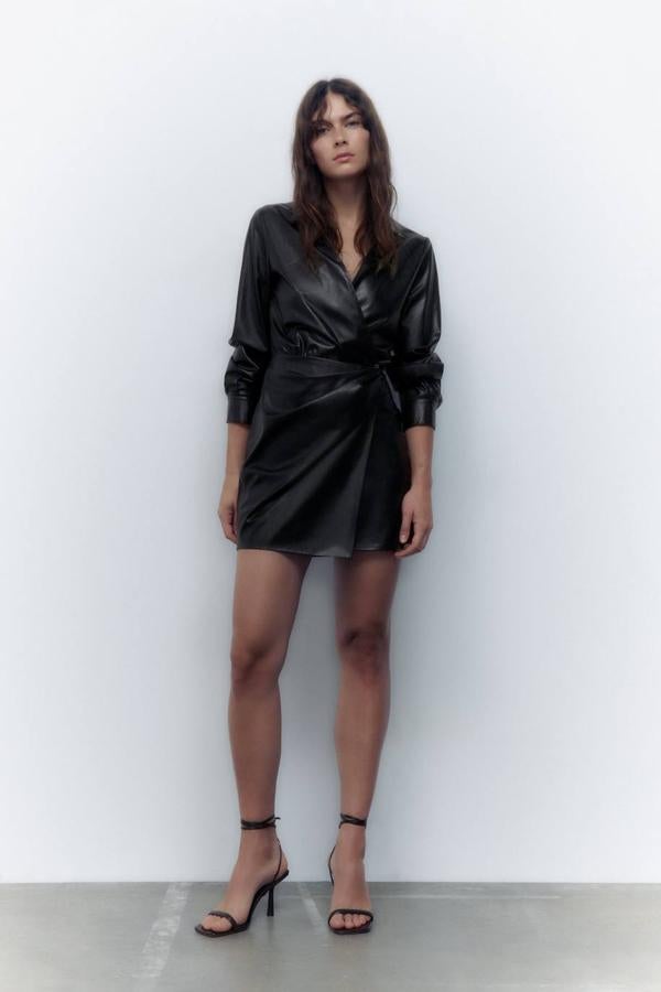 Vestido corto camisero en tejido efecto piel con detalles drapeados, diseño cruzado, manga larga, abertura en el bajo y cuello solapa, en negro, de Zara. Cuesta 35,95 euros.