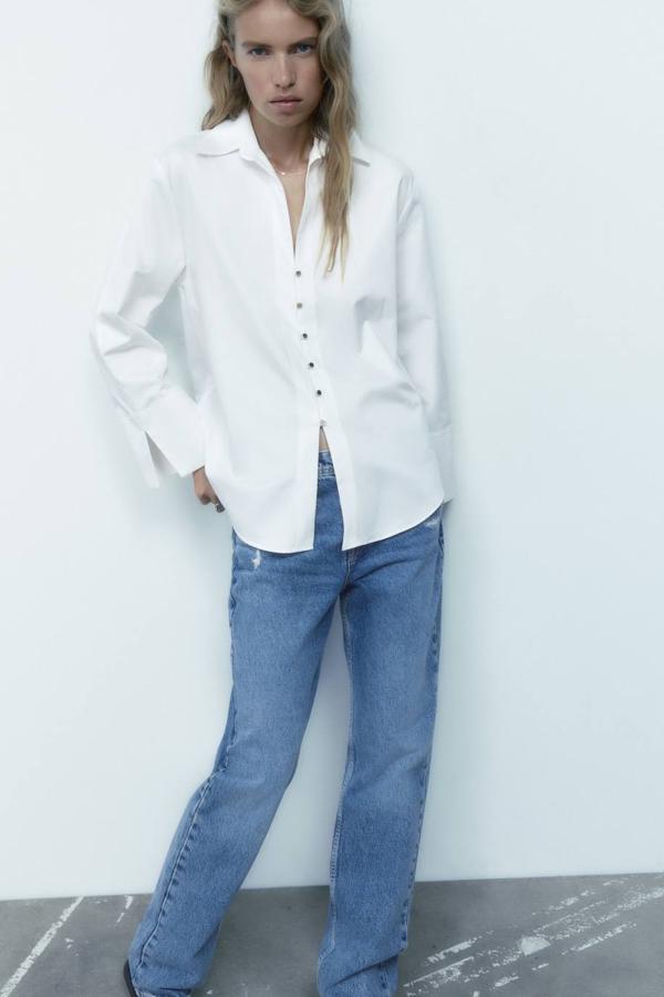 Camisa blanca clásica en tejido de popelín con corte relajado, manga larga, cuello solapa y detalle de botonadura dorada, de Zara. Encuéntrala a 29,95 euros.