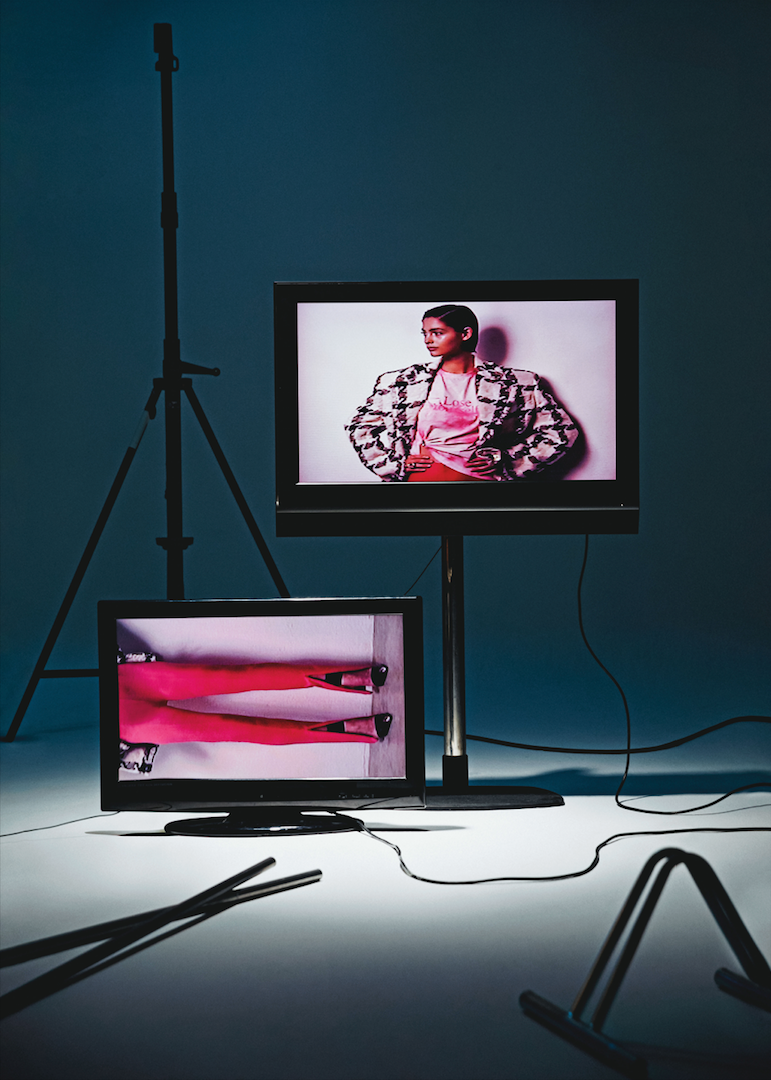 Blazer de tweed, de Versace; camiseta de Peter Saville x Paco Rabanne; anillo de metal y cristal rosa, de Swarovski y maxianillo flor de Tétier Bijoux. En la pantalla de abajo, pantalón elástico de Pinko y zapatos de piel con punta metálica, de Alexander McQueen.