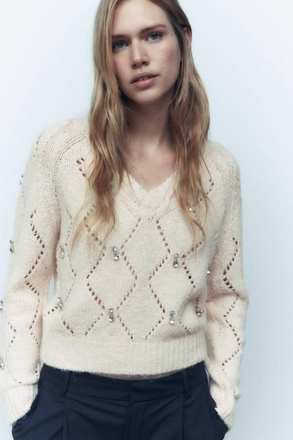 Jersey de punto con patrón calado de rombos, manga larga, escote de pico y aplicación de brillantes, en crudo. Cómpralo a 29,95 euros.