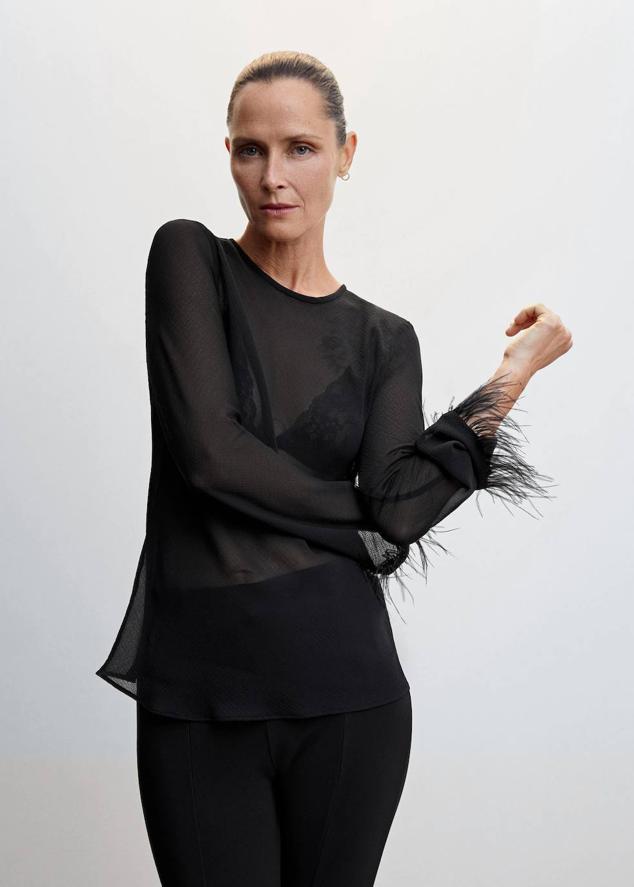 Blusa en tejido semitransparente con cuello redondo, aberturas en la espalda y manga larga con puños de plumas a tono, en negro, de Mango. Puedes comprarla a 39,99 euros.