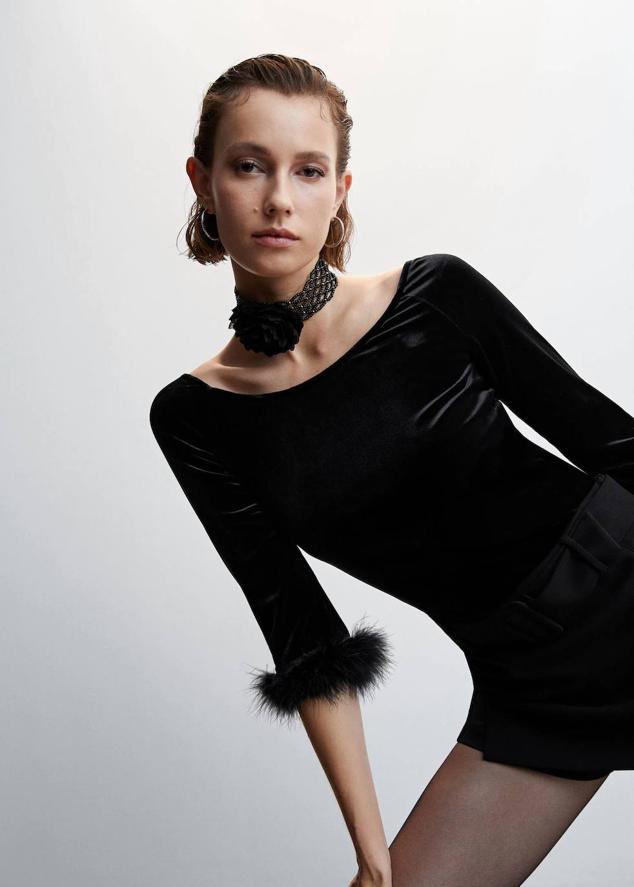 Camiseta en tejido de terciopelo con cuello barco y manga tres cuartos terminada en adorno de plumas, color negro, de Mango. Cuesta 19,99 euros.