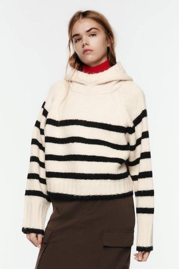 Jersey en tejido de punto grueso con lazada, silueta relajada, manga larga, capucha y print a rayas crudo y negro, de Zara. Su precio es de 39,95 euros.