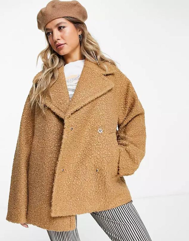 Abrigo corto en tejido bouclé con cuello solapa, manga larga, bolsillos y cierre cruzado, color camel, de Monki. Tiene un coste en Asos de 29 euros.