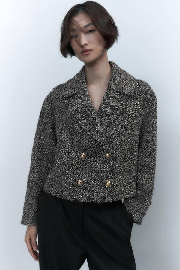 Blazer cropped en tejido de estructura jaspeado, con cuello solapa con muesca, manga larga y cierre de doble botonadura dorada, de Zara. Cómprala a 59,95 euros.