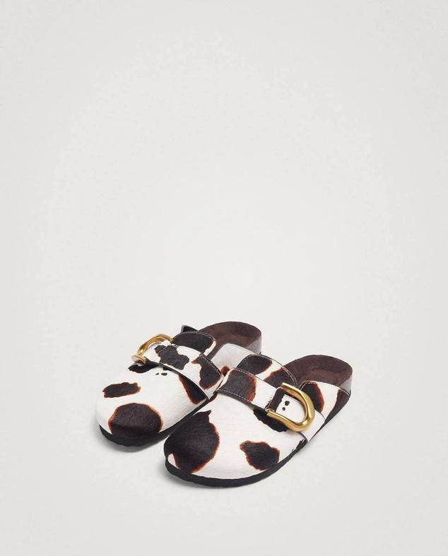 Zuecos planos con diseño destalonado, punta redondeada, detalle de hebilla y tejido de piel con estampado animal de vaca, de Parfois. Están disponibles en El Corte Inglés por 49,99 euros.