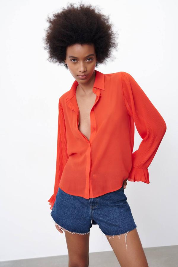 Blusa en tejido ligero con mangas largas plisadas terminadas en volantes, cuello solapa y botones, tono coral, de Zara. Cuesta 15,99 euros, con descuento.