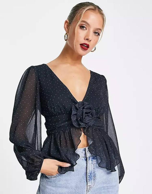 Blusa en tejido vaporoso con manga larga abullonada, escote de pico y detalle de flor en relieve, en print de lunares, de Asos. Te costará 40,99 euros.