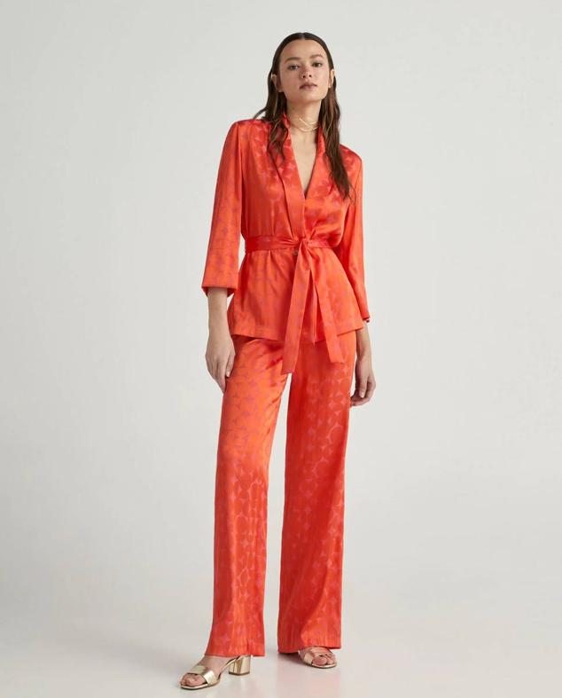 Conjunto en tejido jacquard satinado con blazer con cinturón y pantalón ancho, en estampado geométrico naranja. Puedes comprarlo a 59,99 euros y 49,99 euros.