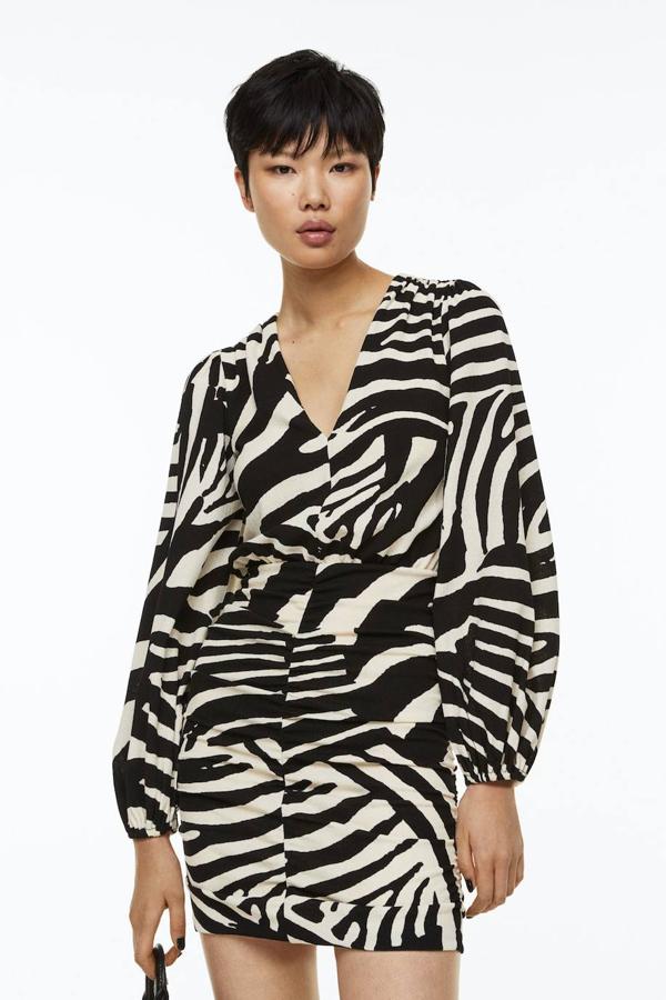 Vestido corto en tejido de punto con escote de pico, manga larga abullonada y detalles fruncidos, en animal print, de H&M. Está disponible por 29,99 euros.