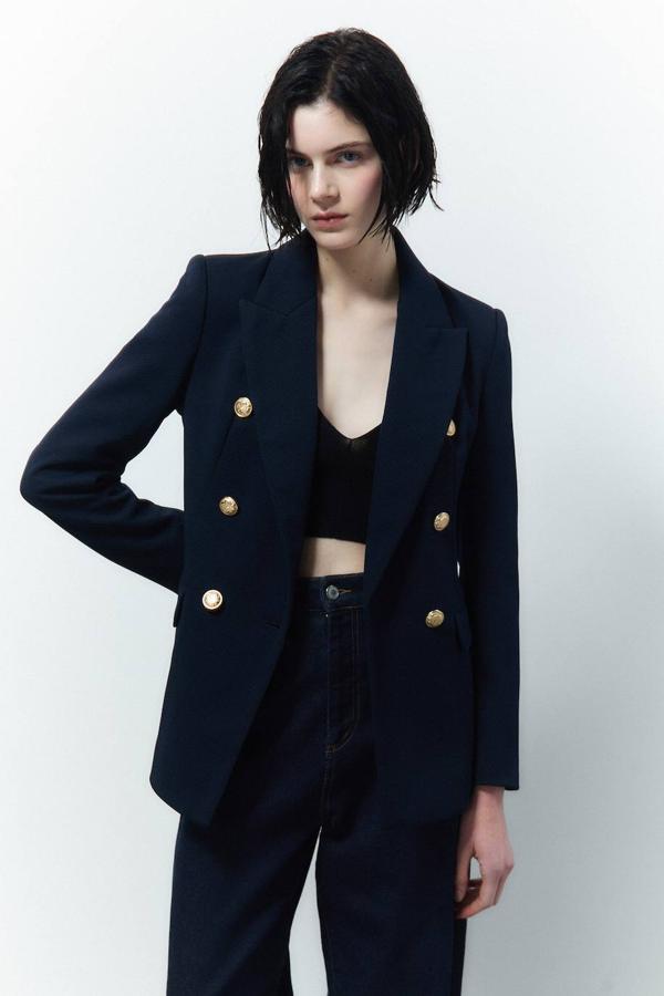 Americana en tejido de piqué con manga larga, cuello solapa puntiagudo y cierre cruzado con doble botonadura dorada, en marino. La encontrarás a 45,99 euros.