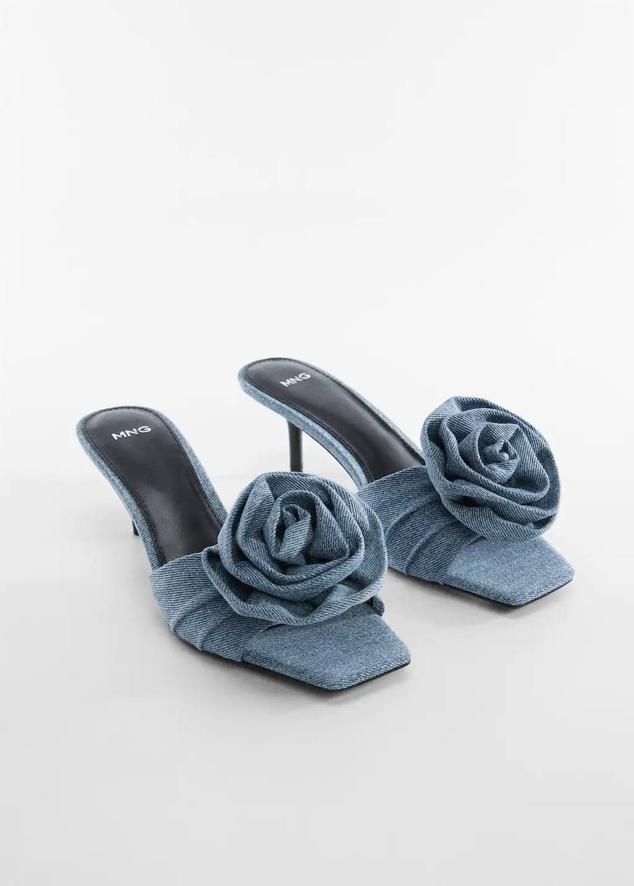 Mules en tejido denim con diseño destalonado, detalle de flor en relieve y tacón bajo, de Mango. Su precio es de 49,99 euros.