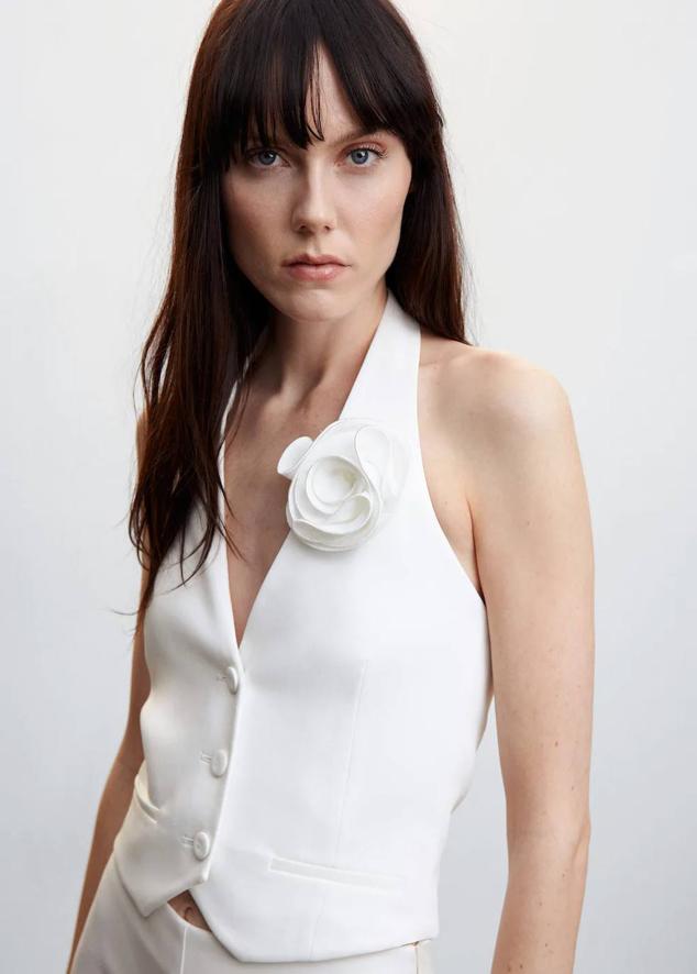 Chaleco de traje con escote halter, espalda al descubierto, diseño entallado, botones a tono y aplique de maxi flor en relieve, color blanco, de Mango. Lo encontrarás a 39,99 euros.