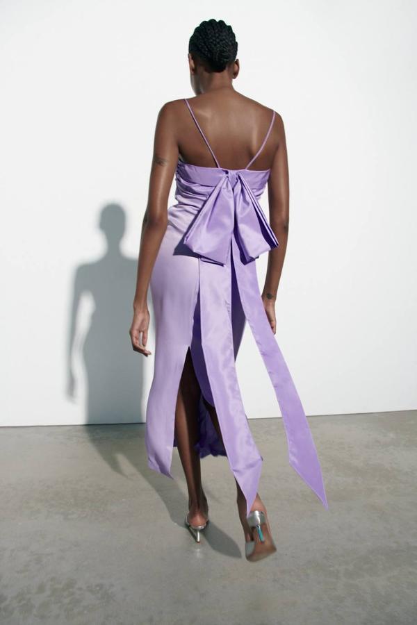 Vestido midi satinado con escote recto con pliegues, tirantes finos, abertura en el bajo y maxi lazo en la espalda, tono lila, de Zara. Consíguelo por 49,95 euros.
