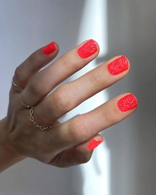Con un pincel, sobre una base natural, roja o de otro color, dibuja lunares o puntos pequeños en toda la uña, en otro tono de rojo como, por ejemplo, neón.
