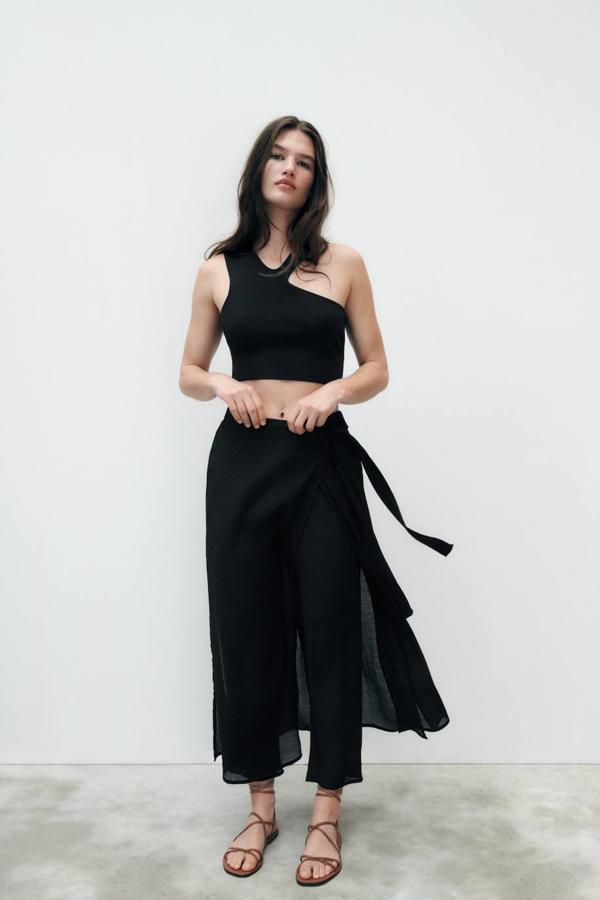 Pantalón pareo en tejido fluido ligero con tiro alto, cintura elástica, pernera holgada y lazada, en negro, de Zara. Lo encontrarás a 29,95 euros.