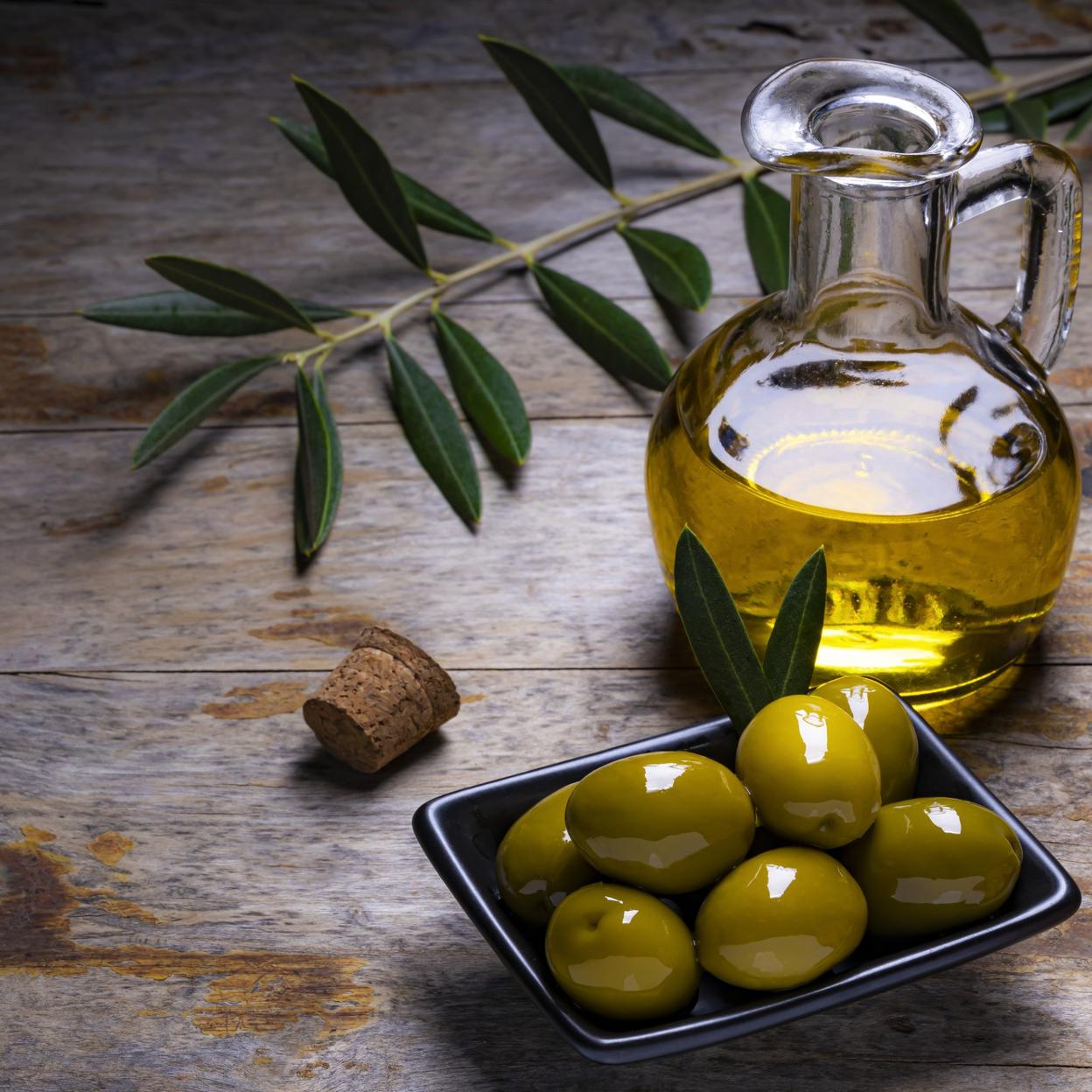 Aceitunas, hojas de olivo y botella de aceite de oliva virgen extra. 