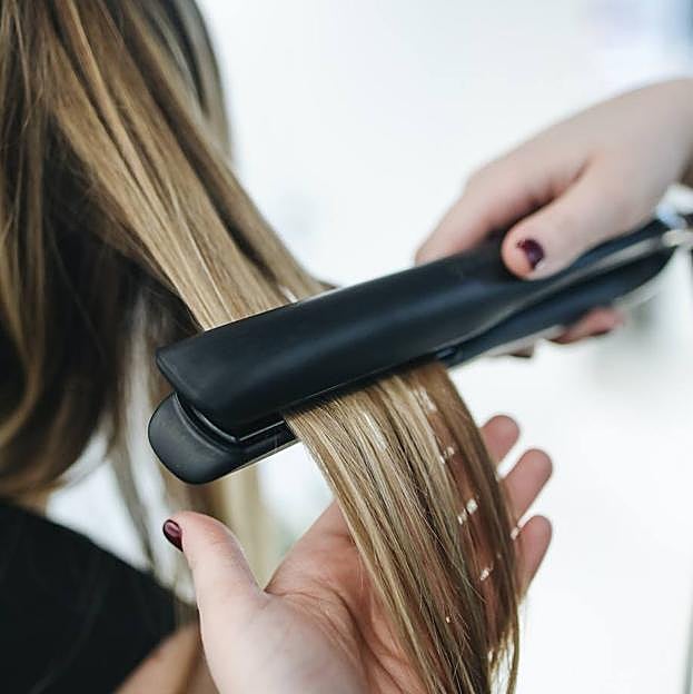 Mujer alisando cabello con la temperatura de plancha de pelo recomendada