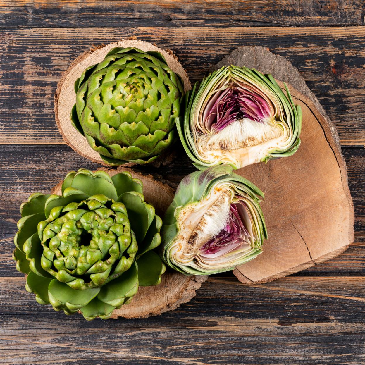 Alcachofas enteras y partidas por la mitad sobre una mesa de madera. 