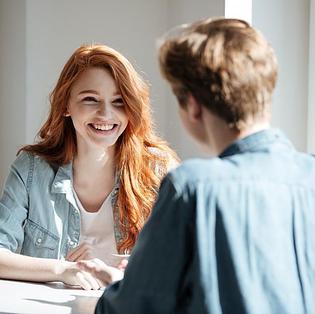 Mujer joven sonriendo mientras conversa con un hombre. 