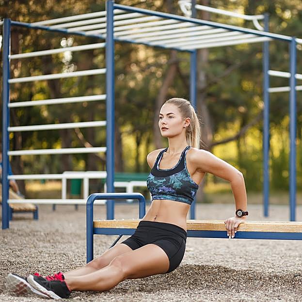 Mujer realizando fondos de tríceps en un parque. 