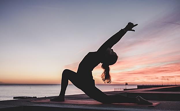 Mujer practicando yoga con el amanecer de fondo. /