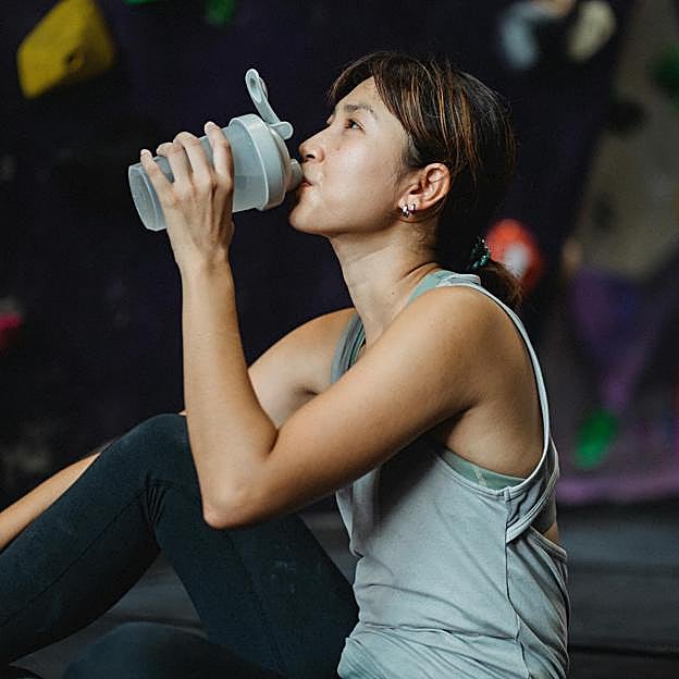 Mujer descansando e hidratándose después de hacer ejercicio. 