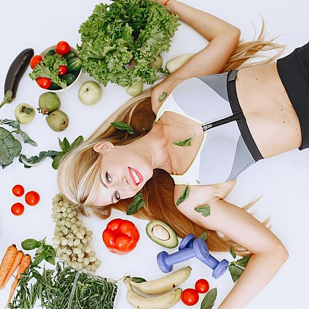 Mujer tumbada en el suelo rodeada de vegetales frescos.
