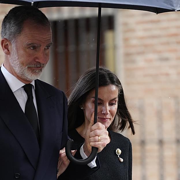 Los reys saliendo del funeral bajo la lluvia.