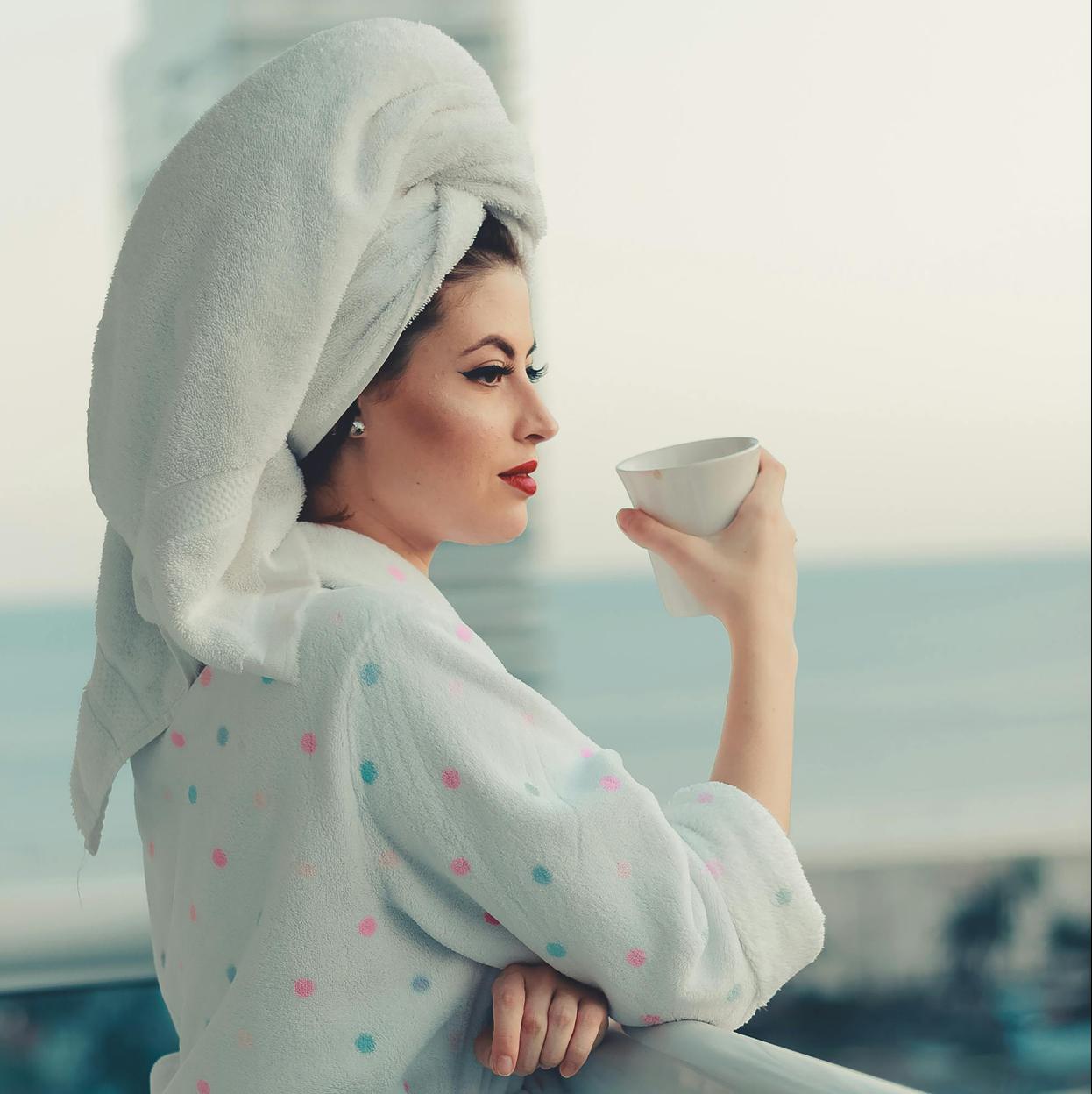 Una mujer en albornoz mirando al mar desayunando