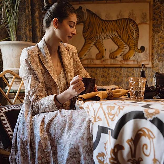 Imagen principal - Conjunto de bata (140 euros) y camisón (95 euros), delantal falda de lino (85 euros); y manta con logo (65 euros). Todo de The IQ Home Collection. 