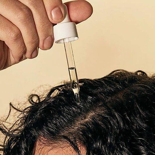 Mujer con pelo rizado aplicando aceite para hacer pre-poo