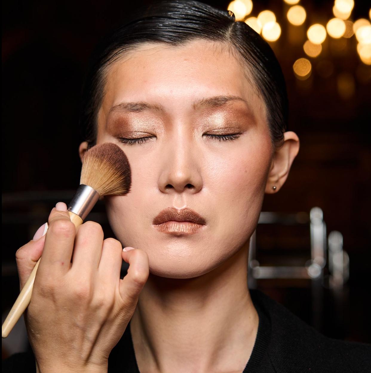 Una modelo siendo maquillajda con brocha.