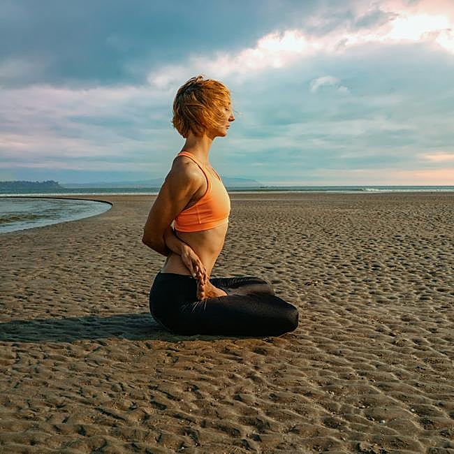 Mujer realizando una postura de yoga en la playa.