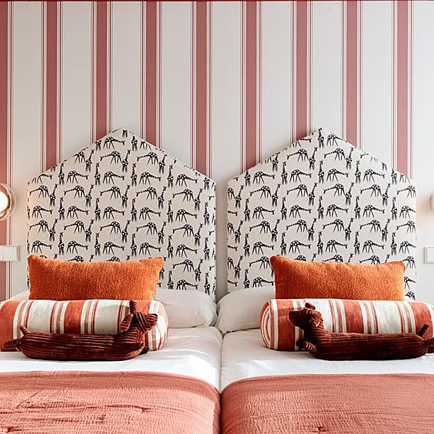 Dormitorio con una original mezcla de papel pintado a rayas y cabecero con estampado de jirafas.