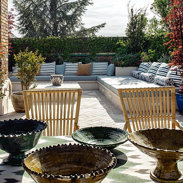 Vista de una de las terrazas, con bancada y mesa de obra y colección de loza de Marrakesh pintada a mano y sillas de médula.
