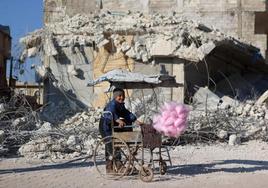 Un niño vende algodón de azúcar junto a la ruinas de la localidad siria de Atarib.