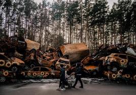 Una pareja y su hijo pasan frente a un cementerio de vehículos destruidos en la batalla de Irpin.