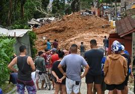 Un grupo de vecinos miran una calle cubierta de lodo en Sao Sebastiao tras las inundaciones