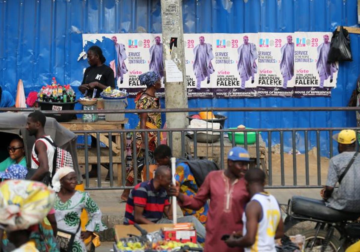 Personas venden sus productos junto a una carretera de la capital de Nigeria en la que se exhiben carteles electorales