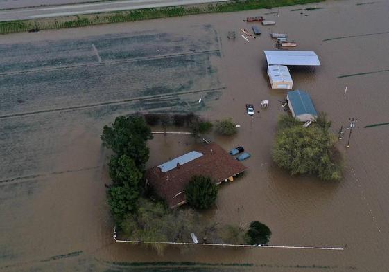 Una imagen aérea muestra una casa, vehículos y tierras de cultivo inundados durante una tormenta en el condado de Tulare, en California.