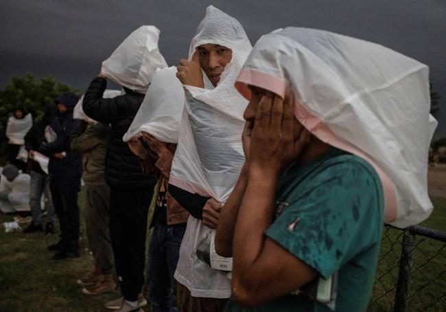 Dos ciudadanos chinos se protegen de la lluvia y el viento con bolsas plásticas mientras esperan que los lleven a un centro de detención en Texas