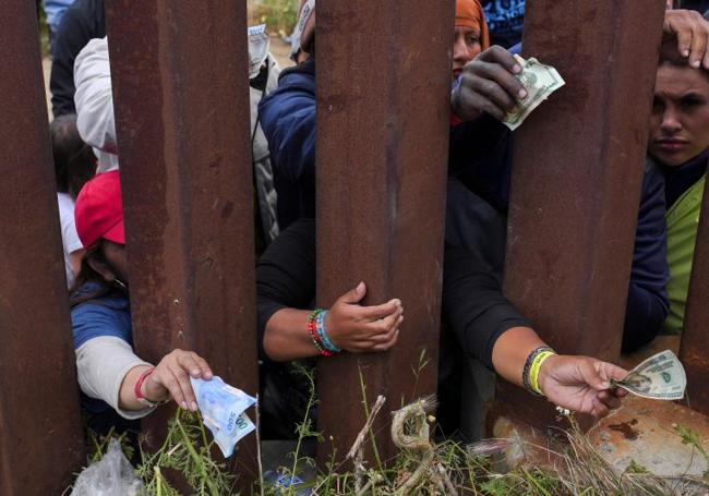 Inmigrantes que esperan al otro lado del muro intentan comprar comida.