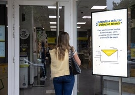 Una mujer entra en una oficina de Correos en la que se informa del voto postal para los comicios de este mes de mayo