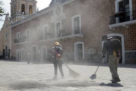 Dos personas barren grandes cantidades de ceniza expulsada por el volcán Popocatépetl en Puebla