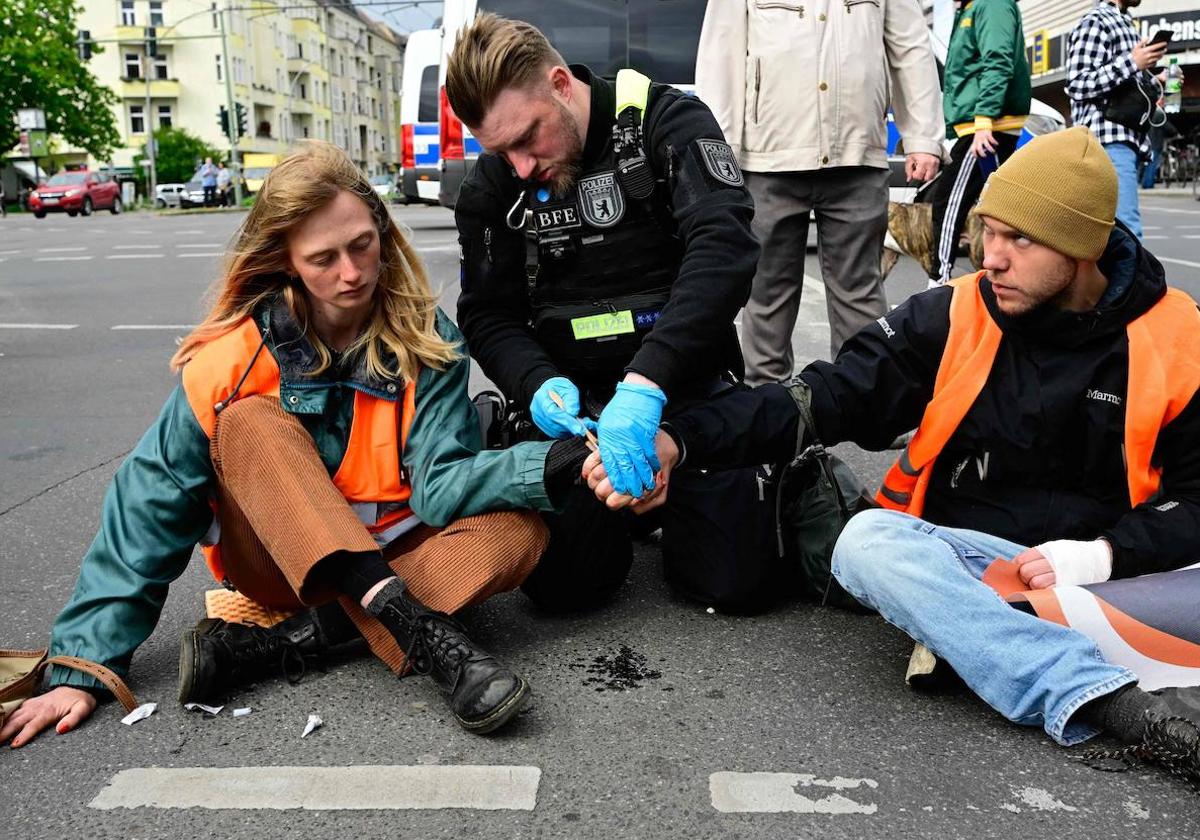 Un oficial de Policía intenta separar las manos de activistas del grupo ecologista 'Última Generación' que se habían pegado al asfalto en señal de protesta en Berlín