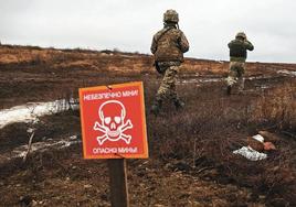 Dos militares caminan por un sendero seguro abierto en un campo minado.