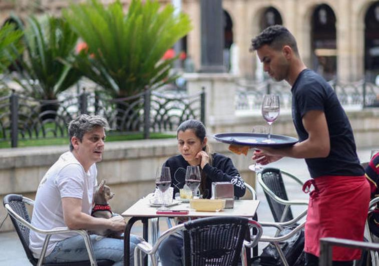 Unos clientes y un camarero en la terraza de un bar.