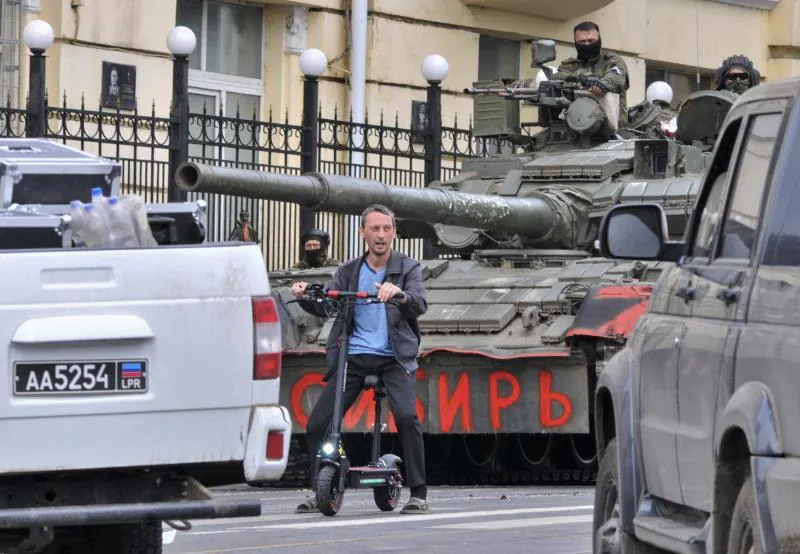 A civilian moves through Rostov on a scooter in front of a tank.