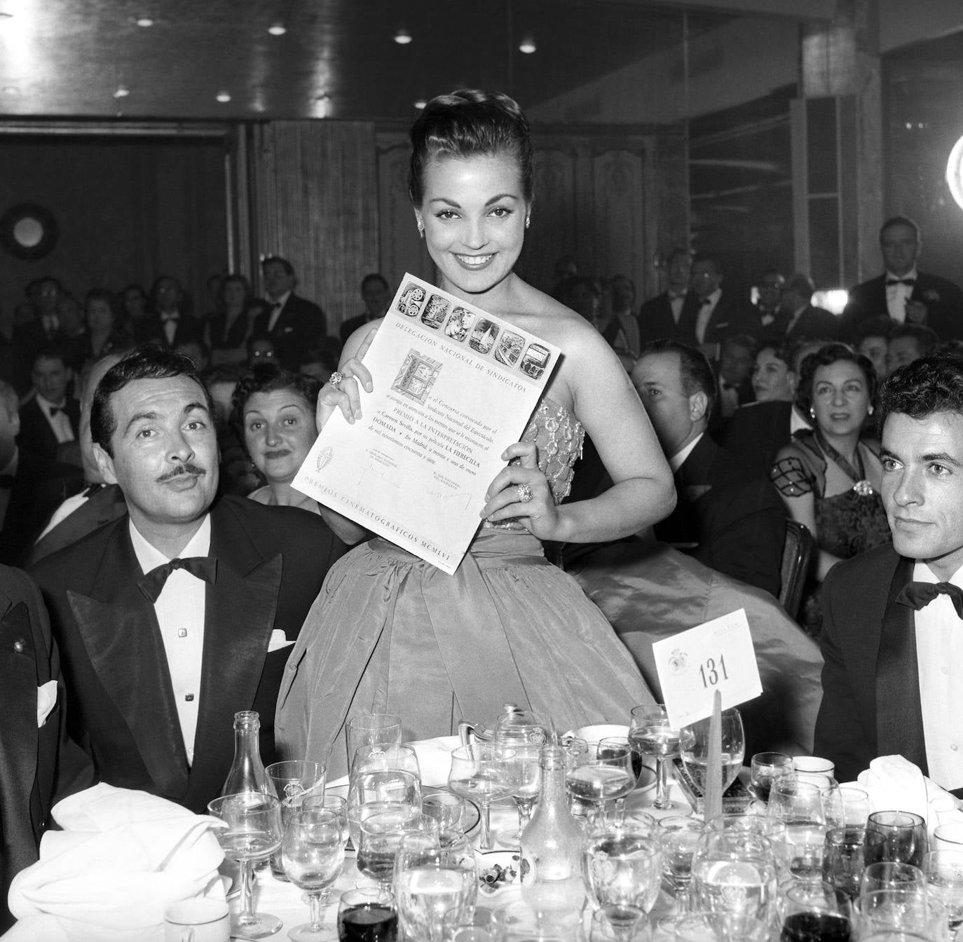 La actriz, acompañada por el actor Juan Calvo (i), recibe el premio de Cinematografía española 1956 por 'La fierecilla domada', durante la cena celebrada en el Hotel Palace de Madrid.